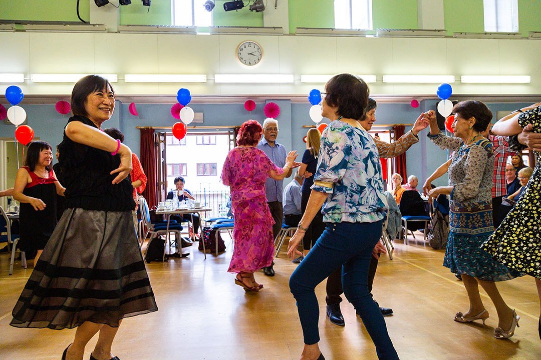 A dancing event at a community space. There are various women dancing, and the space is decorated with balloons.