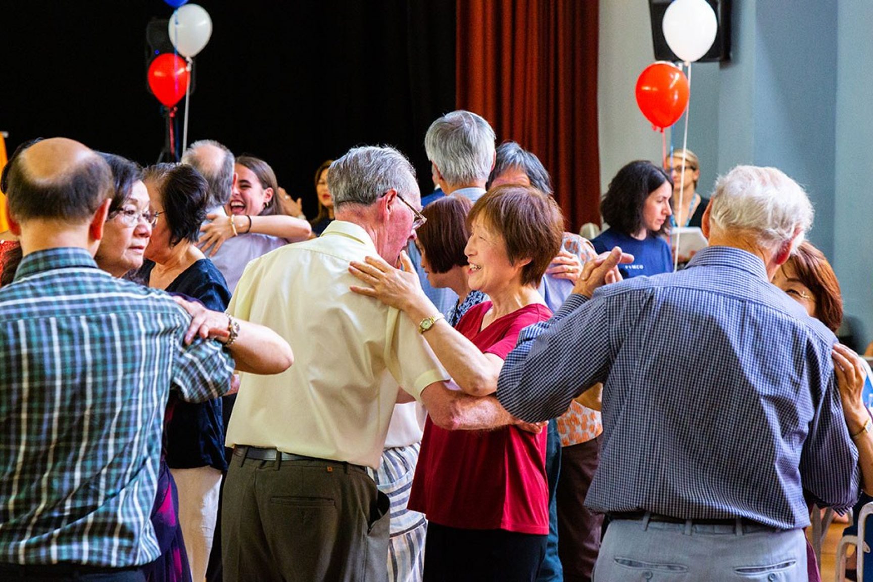 There are older couples dancing at a community space. Balloons are decorating the space.