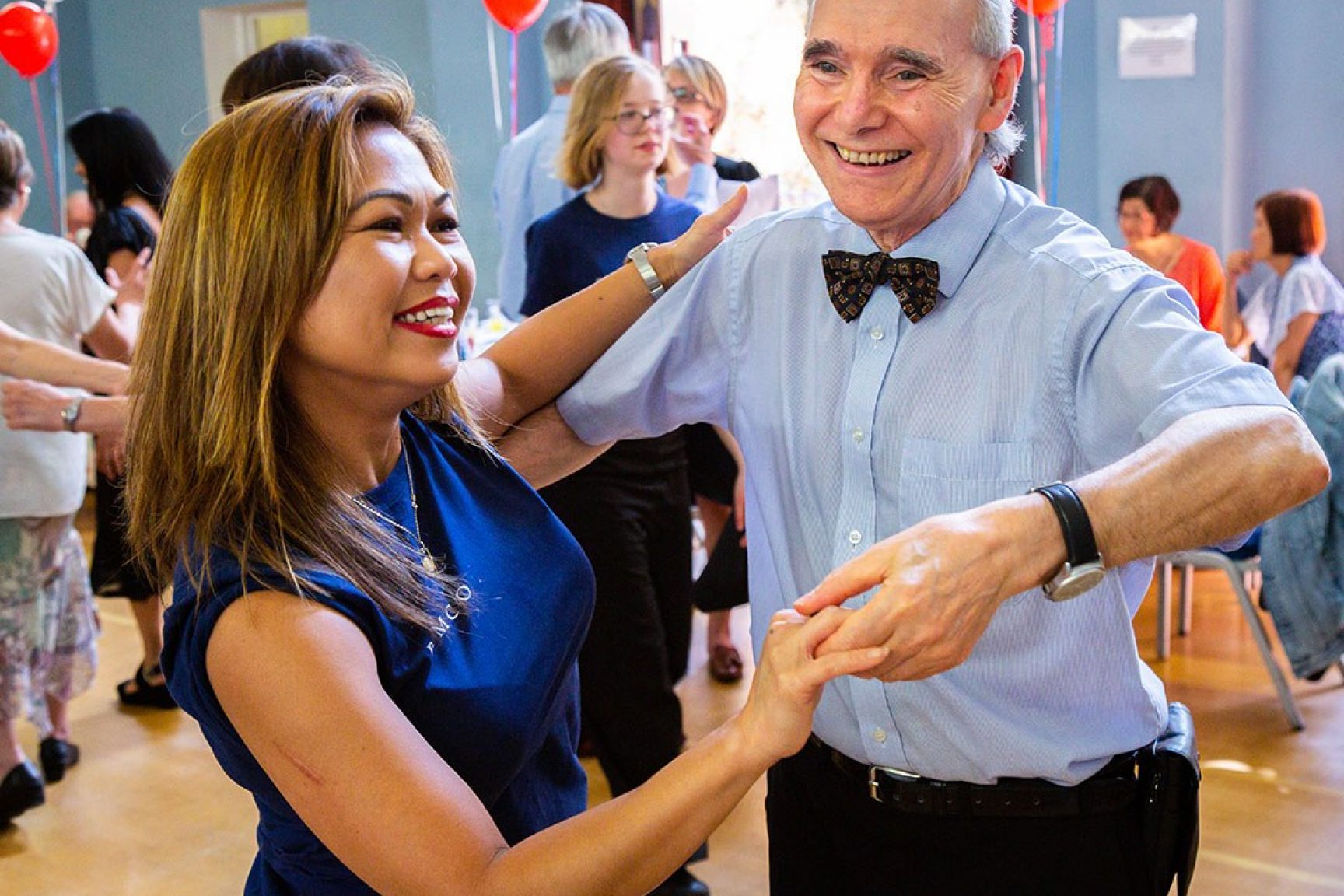 A female volunteer is dancing with an older man at a community event, they are both smiling and having fun.