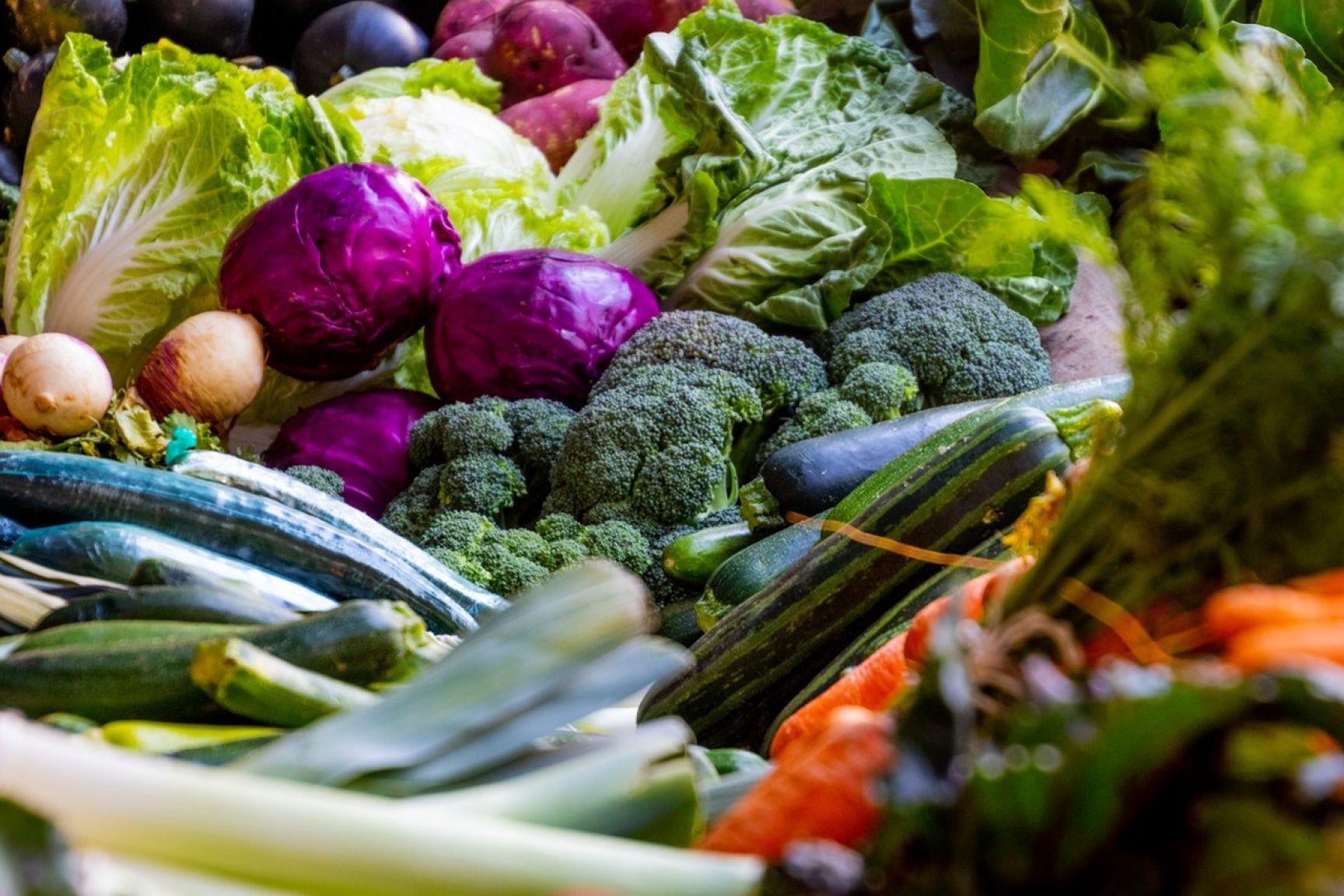 Lots of vegetables are spread out beautifully on a table, there is broccoli, cabbage, leeks, courgette, potatoes and more.