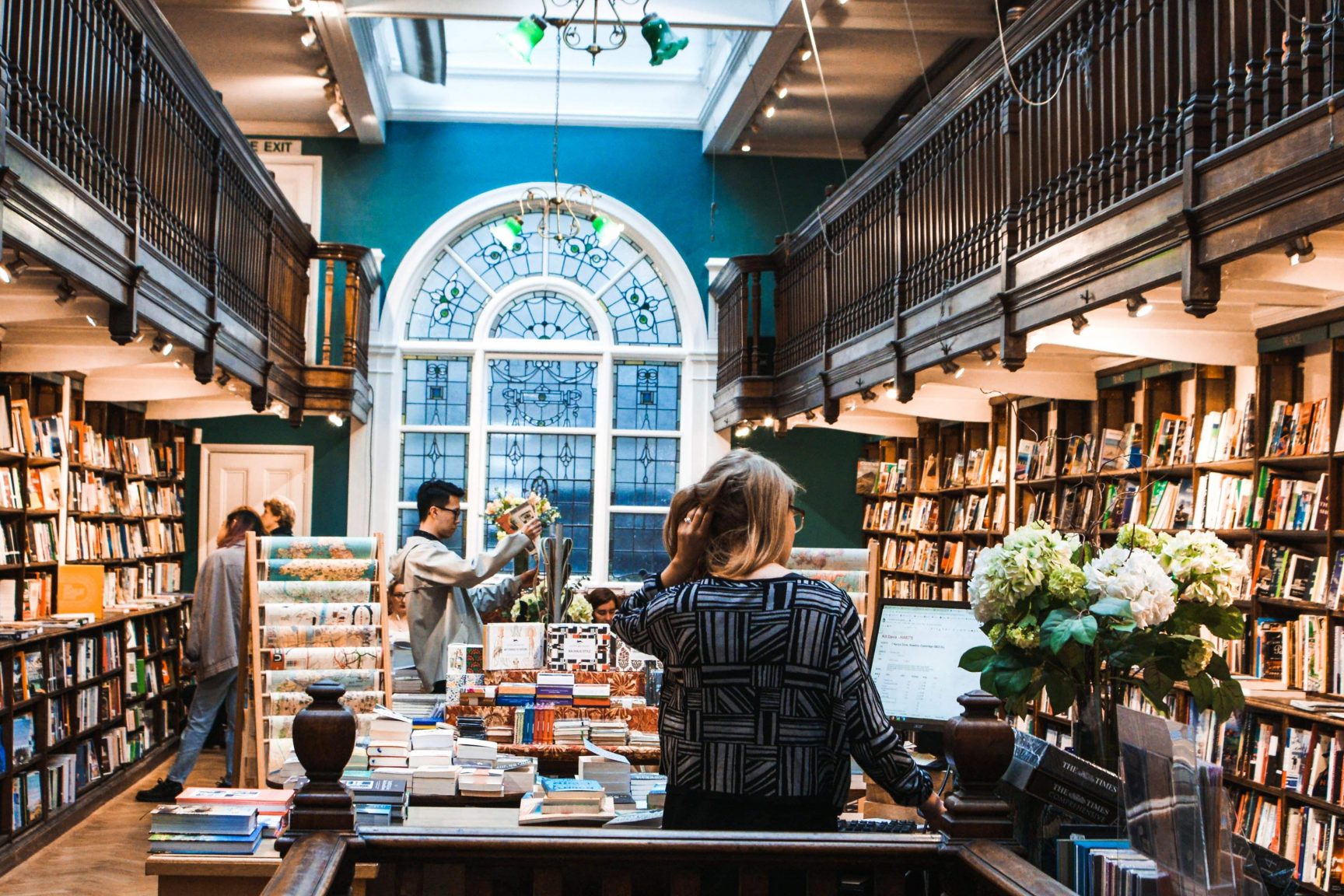 A shop selling books and gifts in a large building with an ornate window with stained glass.
